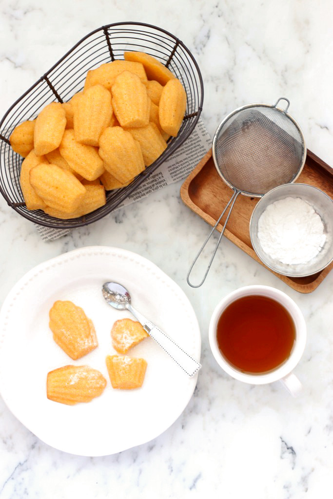 A basket of cornbread madeleines and a cup of tea on a marble board.