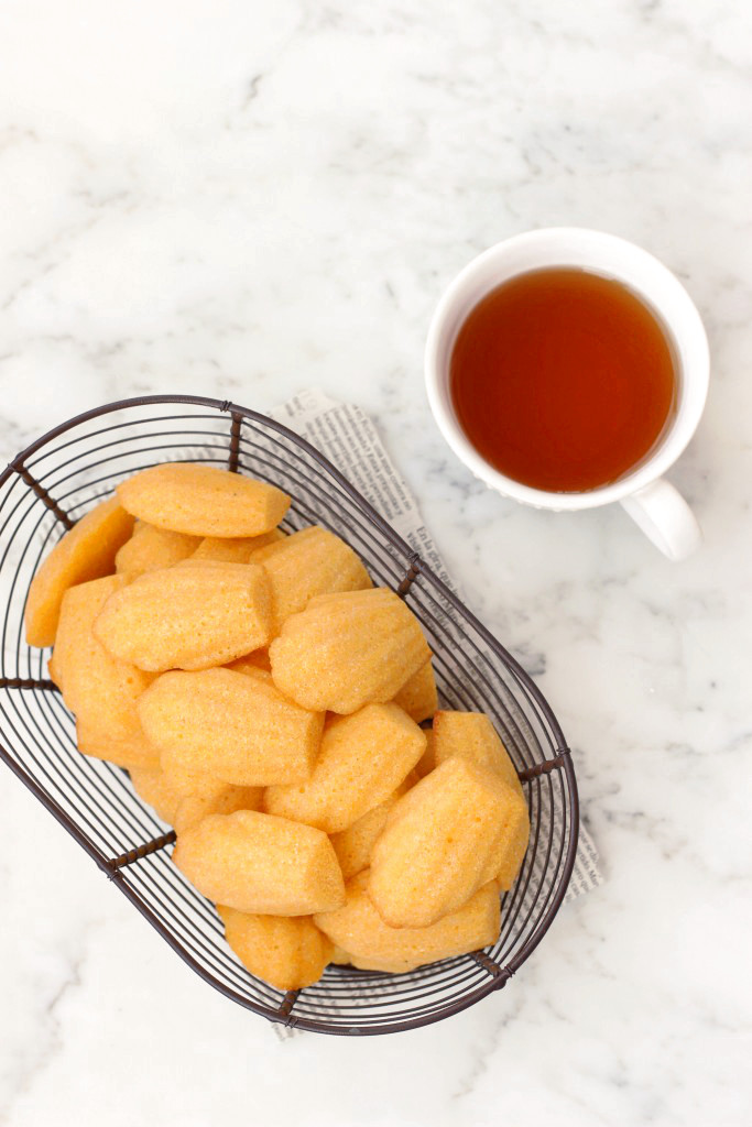 A wire basket of cornbread madeleines and a cup of tea on a marble board.
