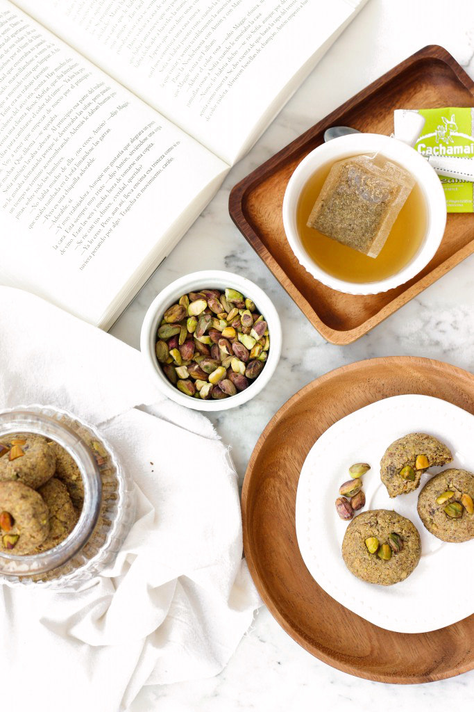 A plate of pistachio cookies next to a jar with a book on marble board.