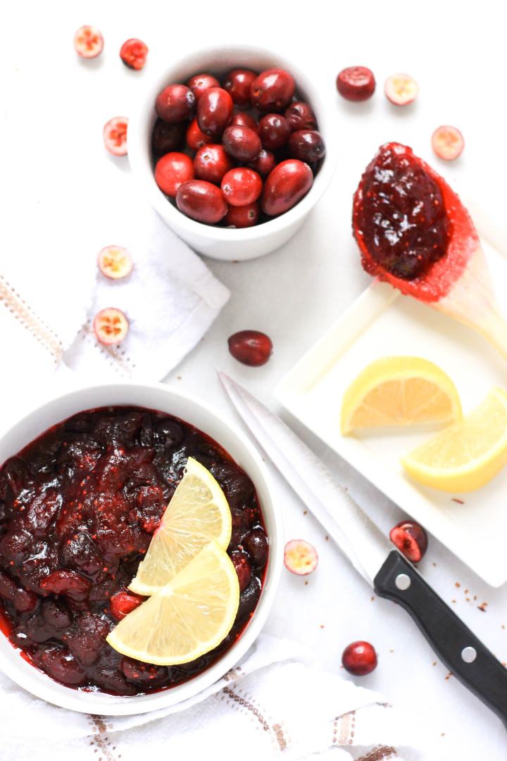 Fresh cranberries, lemon slices and a bowl of cranberry sauce on the table.