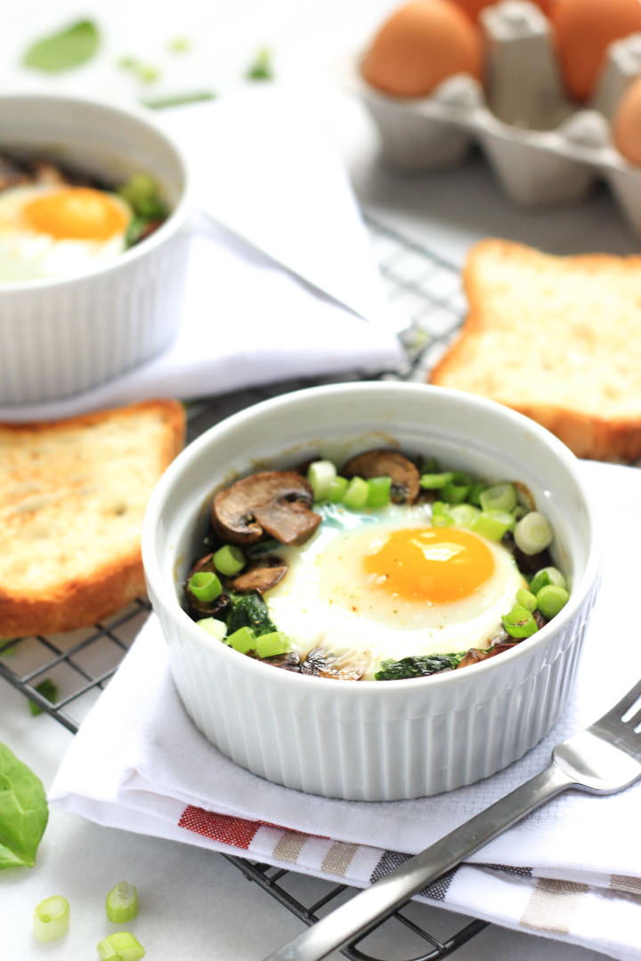 Up close shot of baked eggs with spinach and mushrooms in a ramekin.