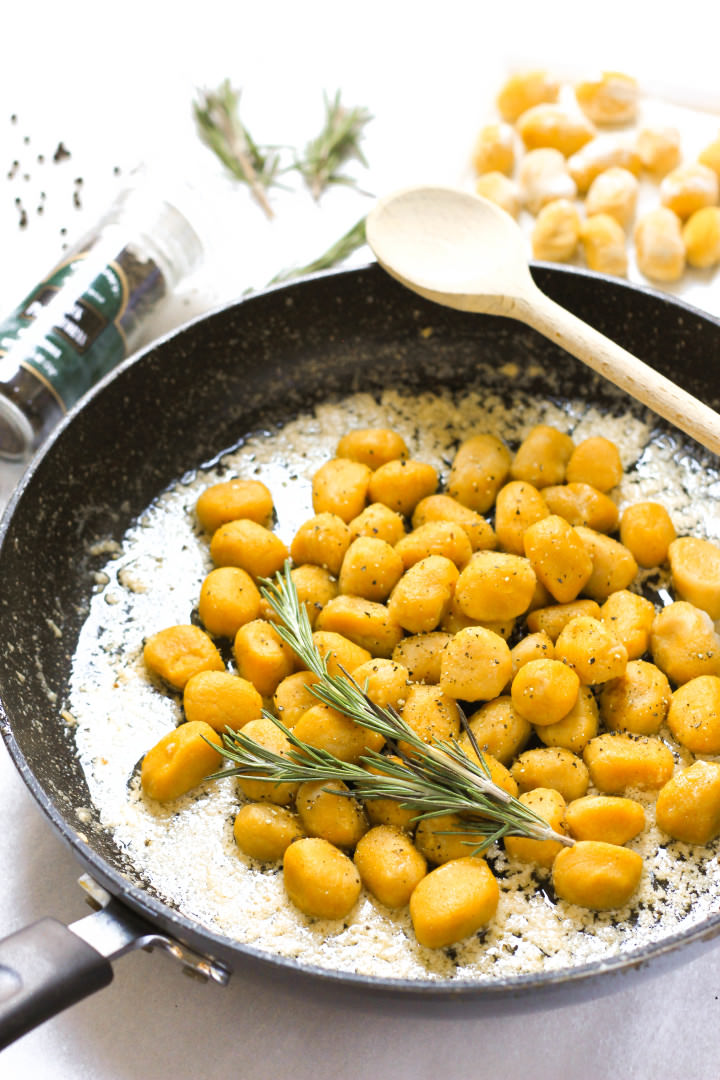 A sprig of rosemary on gnocchi in a pan.