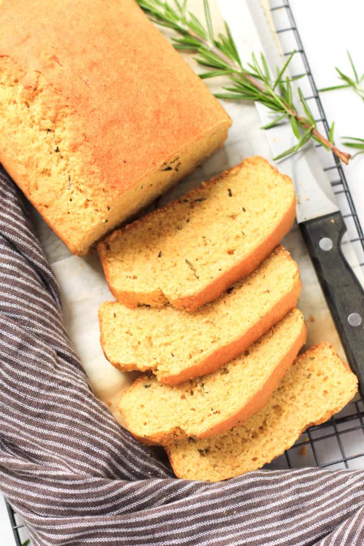 A sliced loaf of cornbread with a kitchen towel at the side.