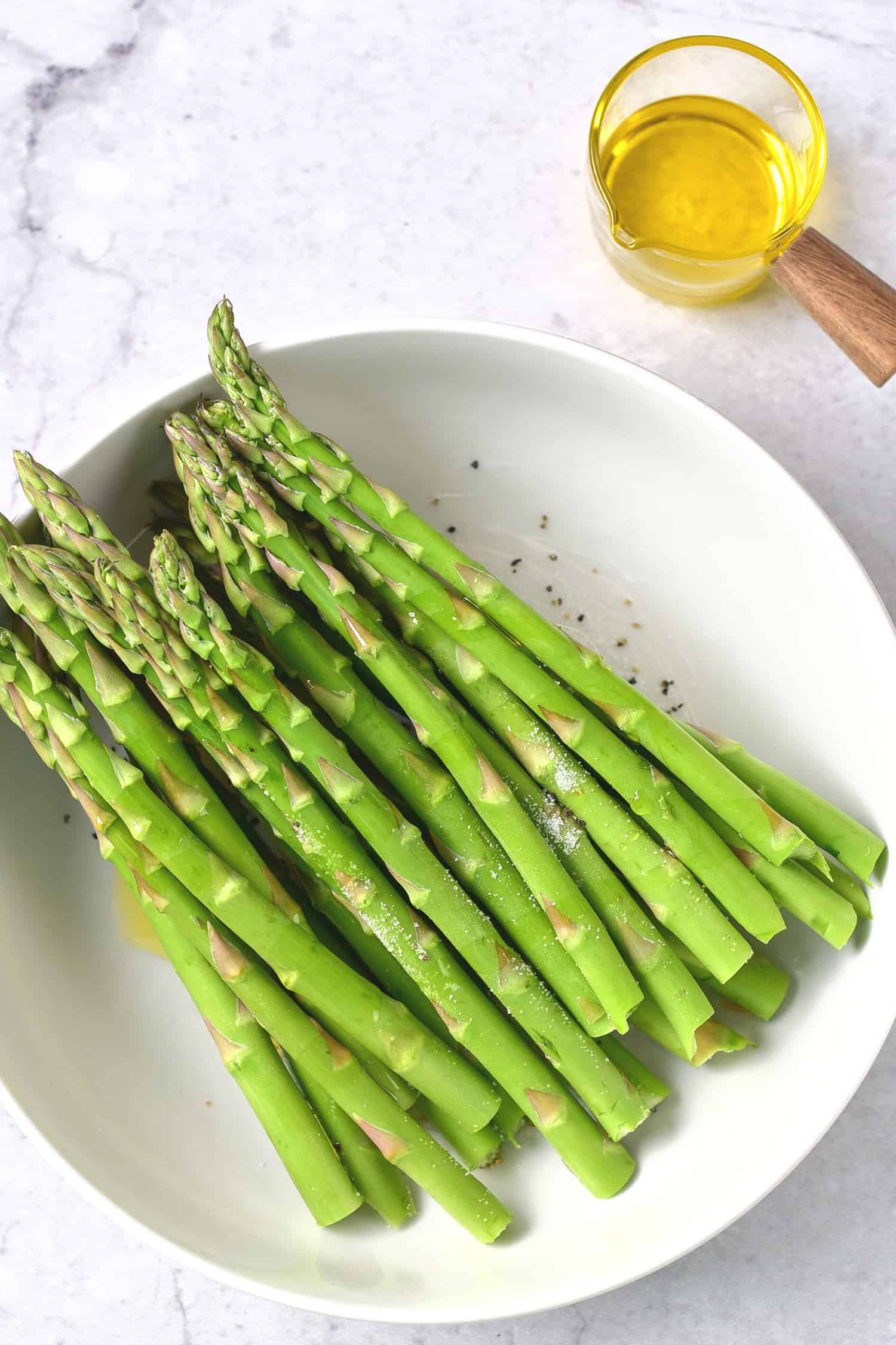 A bowl of asparagus stalks and olive oil.