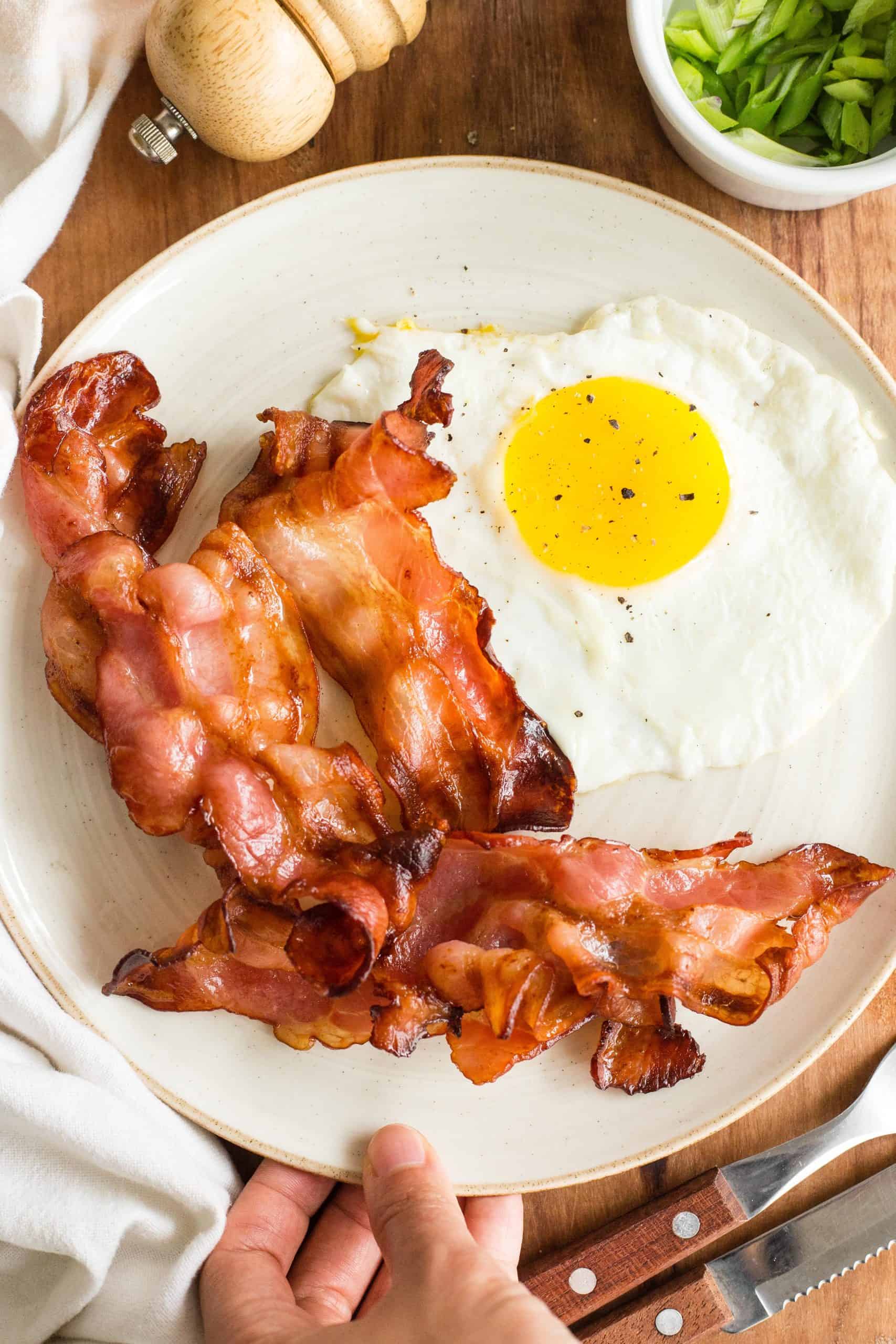 Hand holding a plate with air fried bacon and eggs.