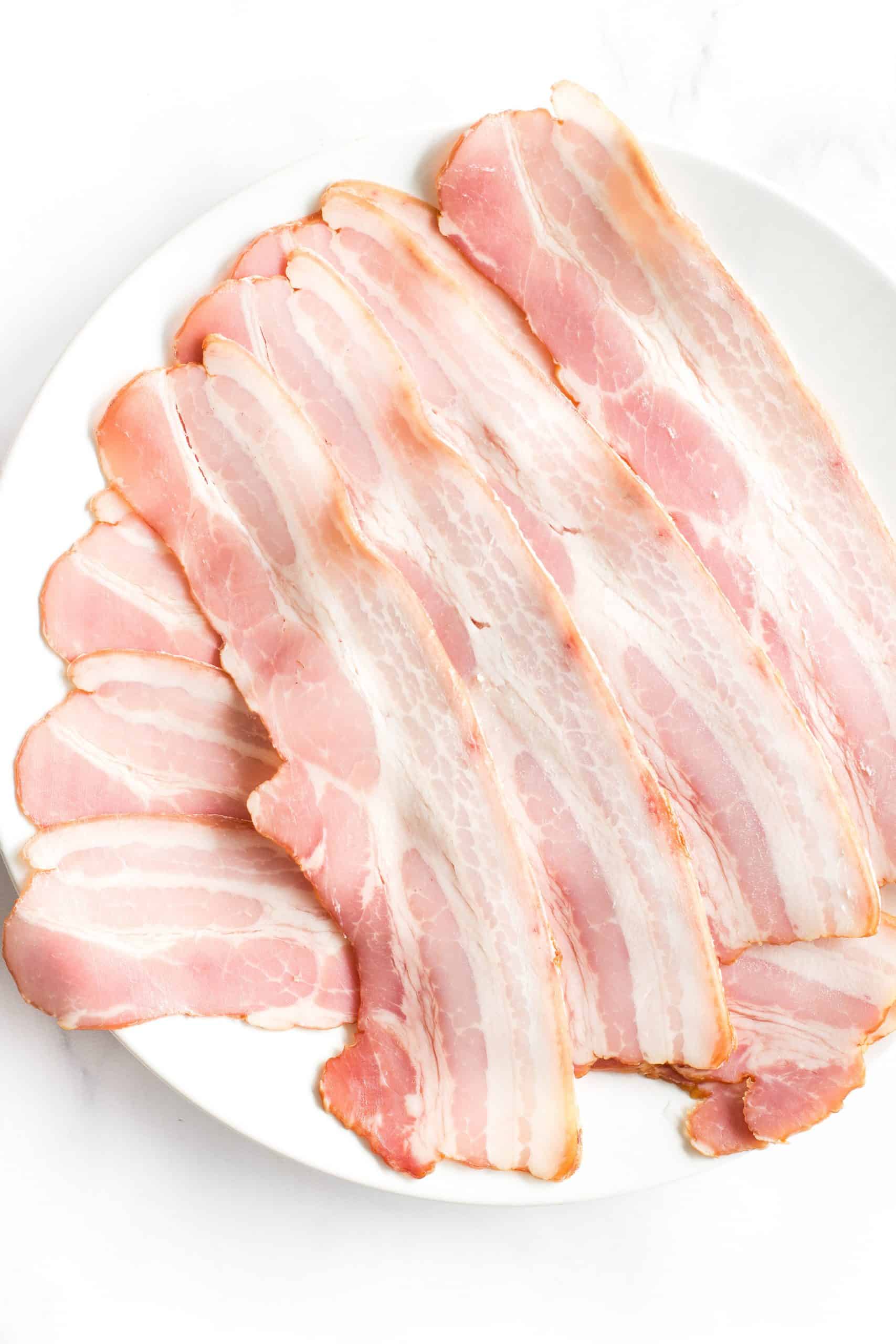Uncooked bacon slices on a white plate.