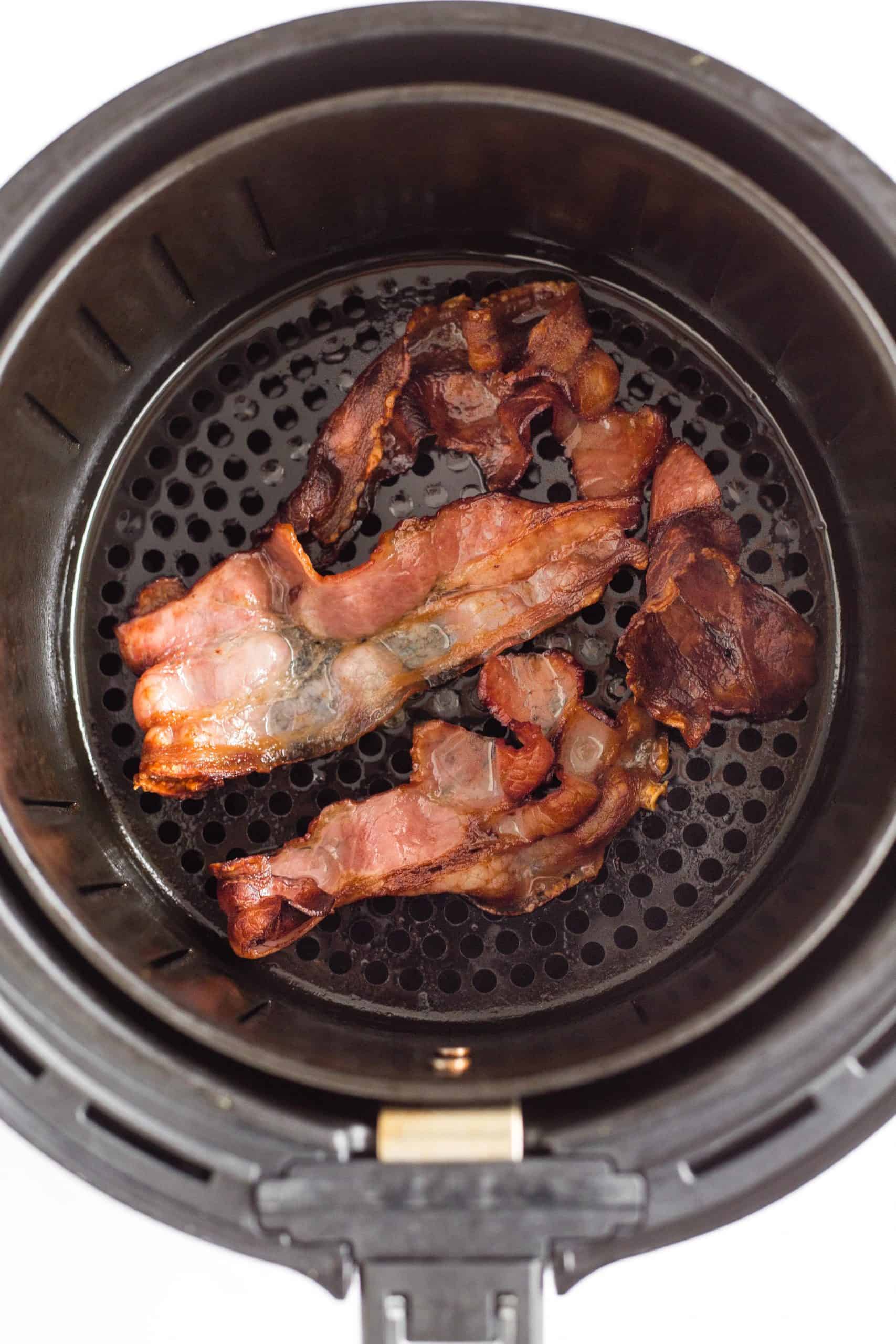 Crispy air fryer bacon slices in the air fryer basket.