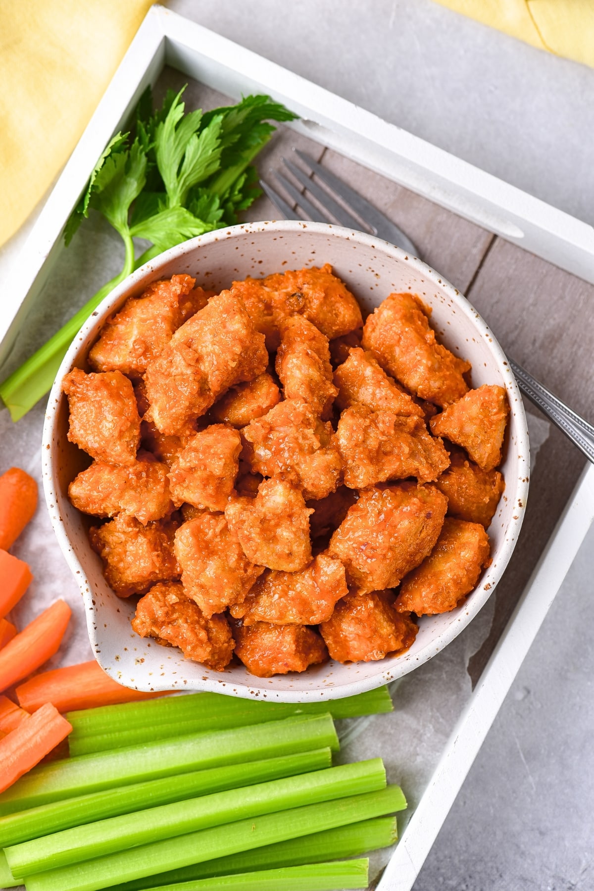 A bowl of buffalo chicken bites and carrot sticks and celery sticks.