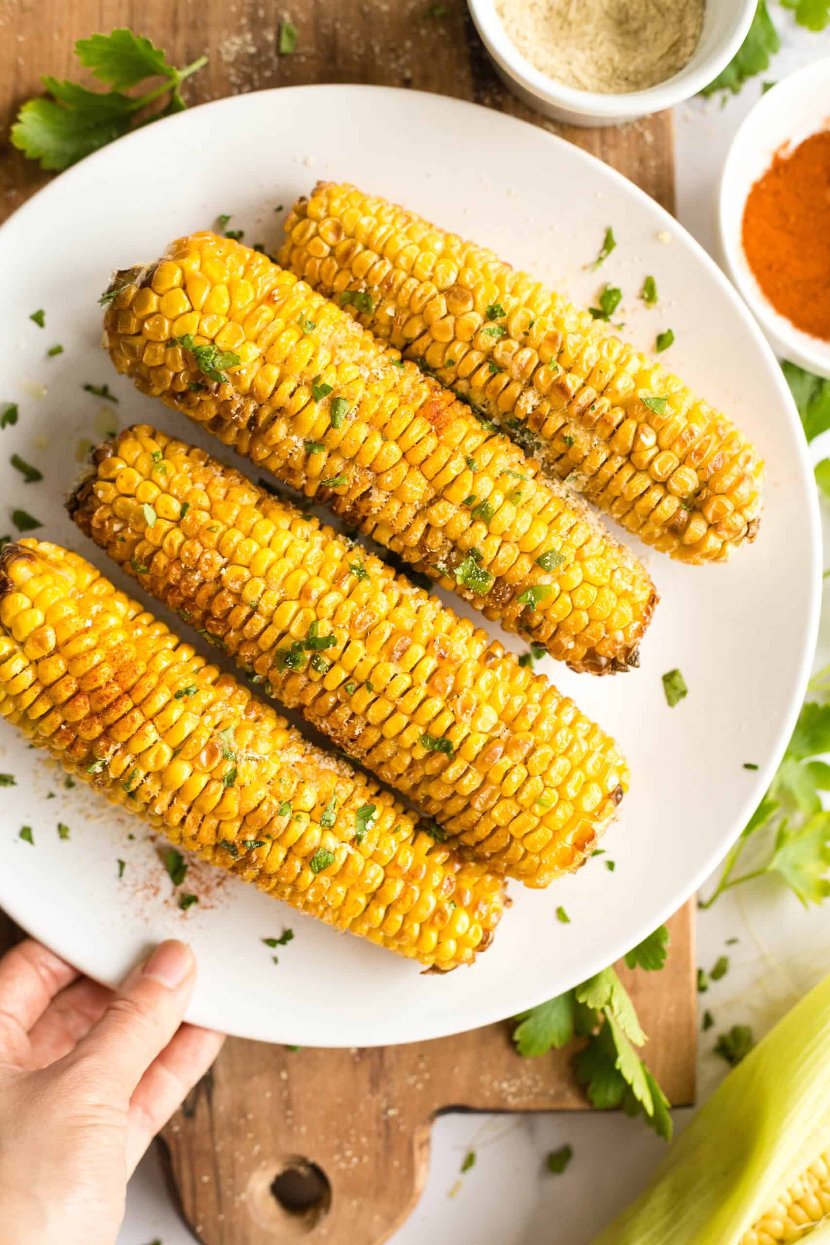 Hand holding a plate of freshly cooked corn on the cob on top of a wooden board.