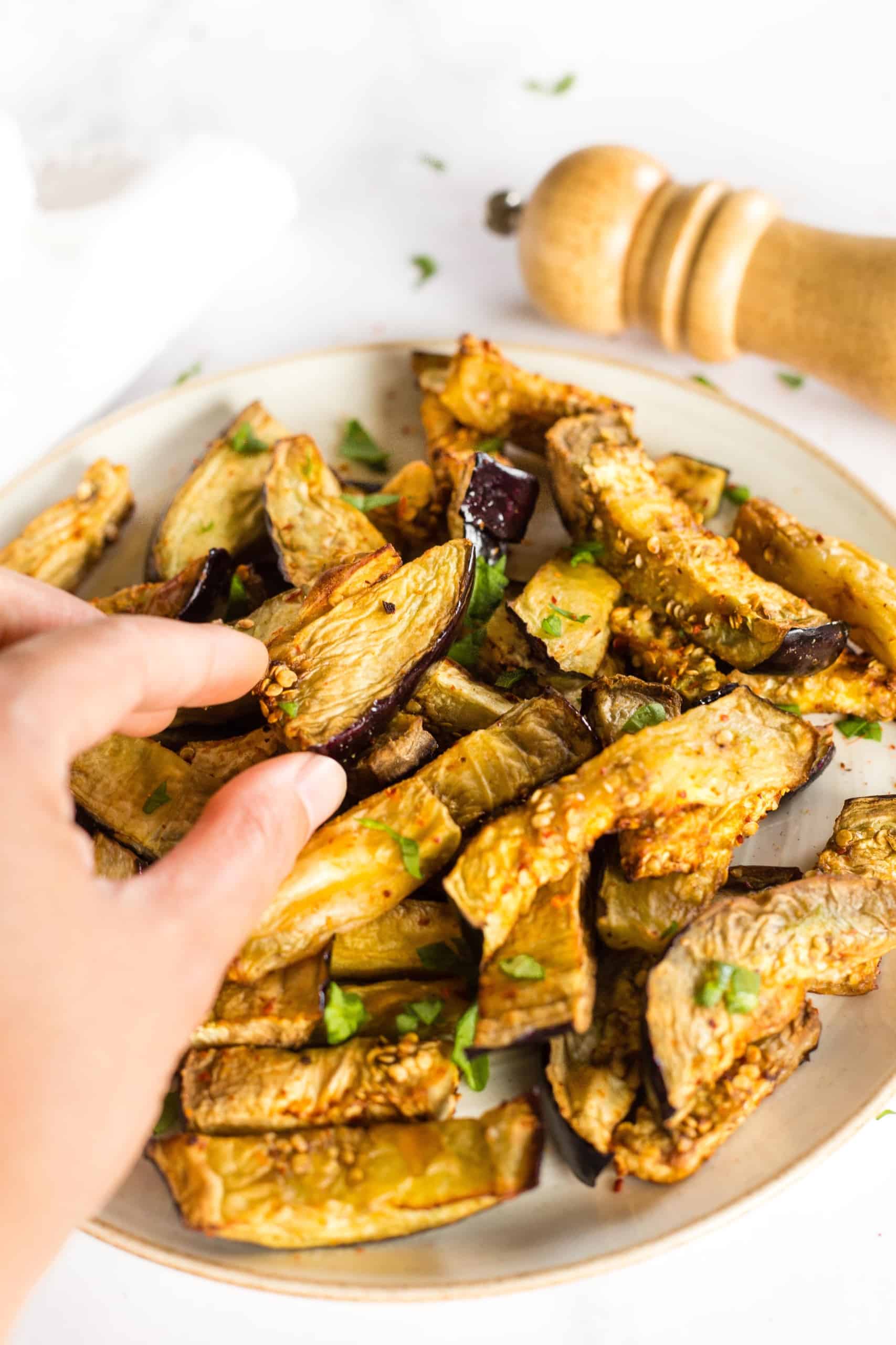 Hand reaching for a piece of air fried eggplant.