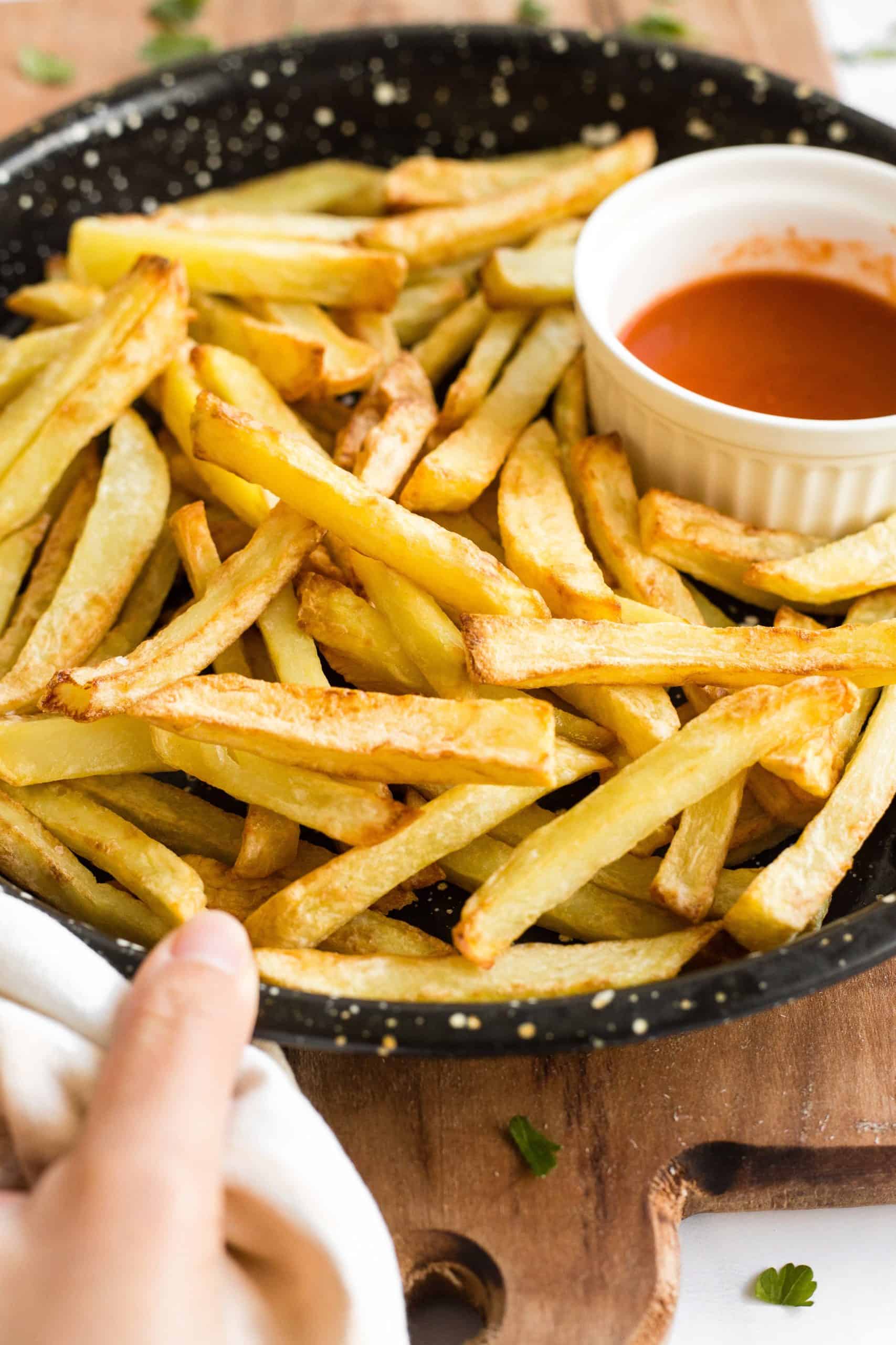 Hand holding a plate of crispy air fryer fries.