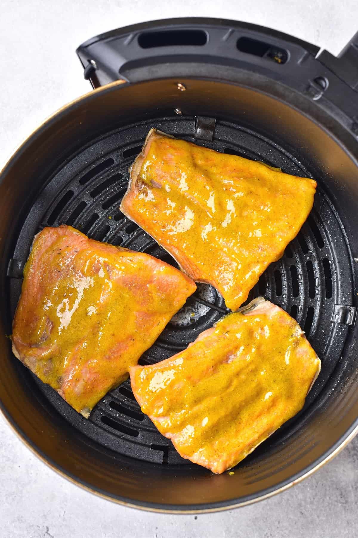 Salmon fillets brushed with yellow marinade in air fryer basket.