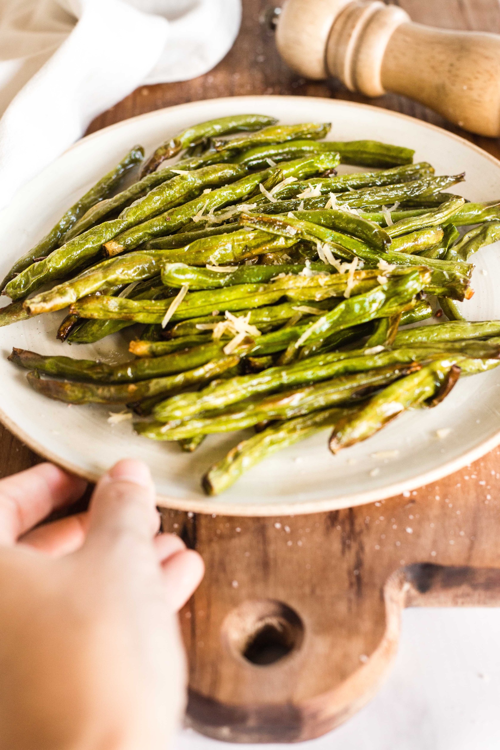 Reaching for a plate of air fryer green beans on a wooden board.
