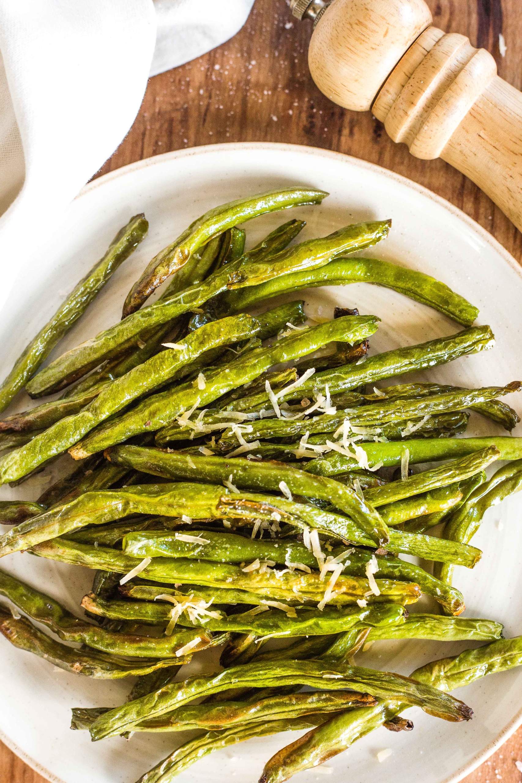 Air fryer green beans on a plate sprinkled with dairy-free shredded cheese.