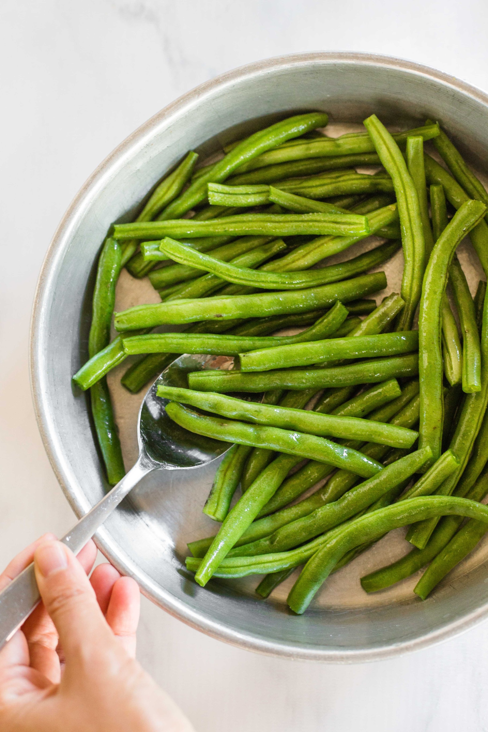 Tossing green beans with oil in a metal bowl.