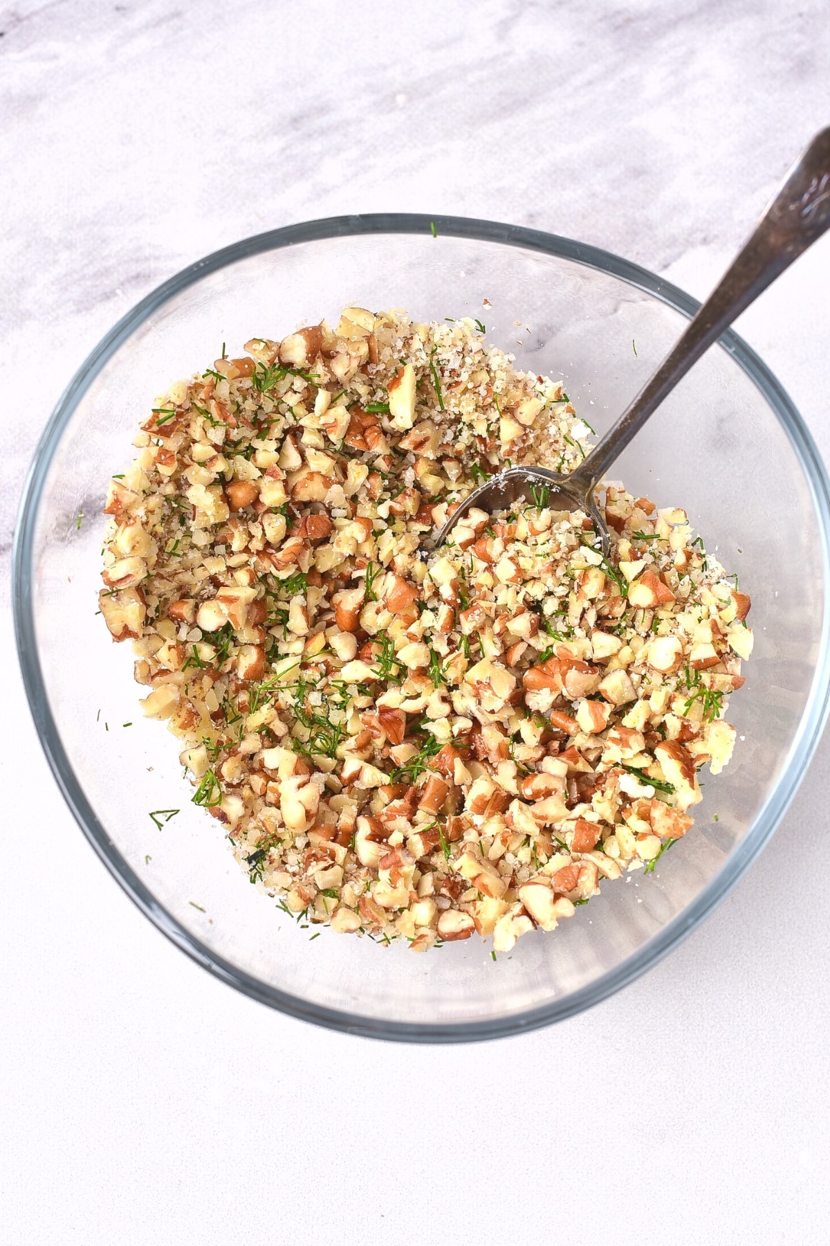 Chopped almonds with herbs in glass bowl.