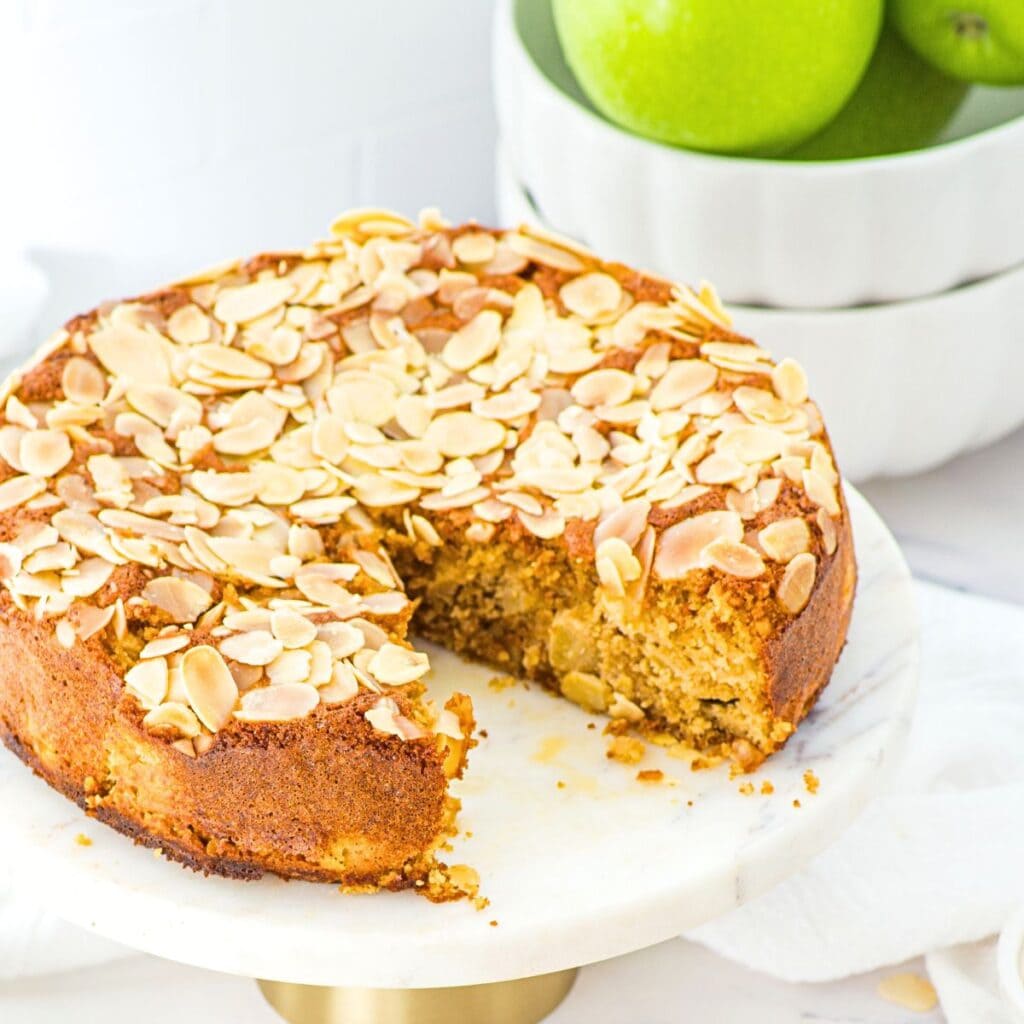 Half-eaten almond flour apple cake with green apples in background