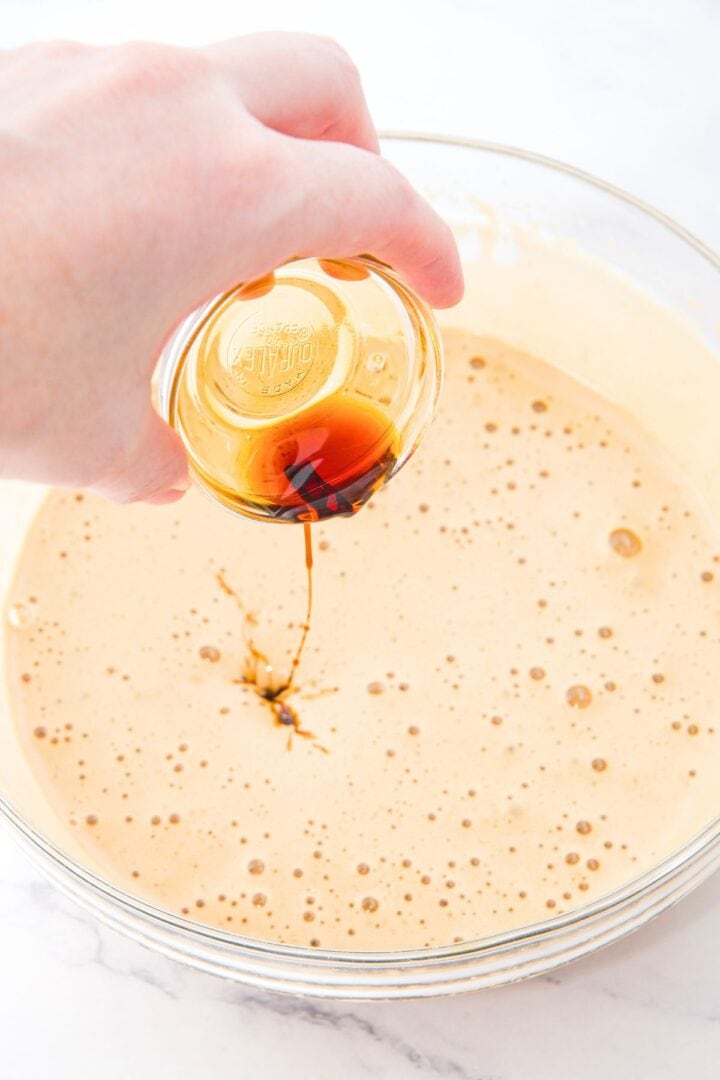 Pouring vanilla extract into a pale yellow cake liquid mixture.