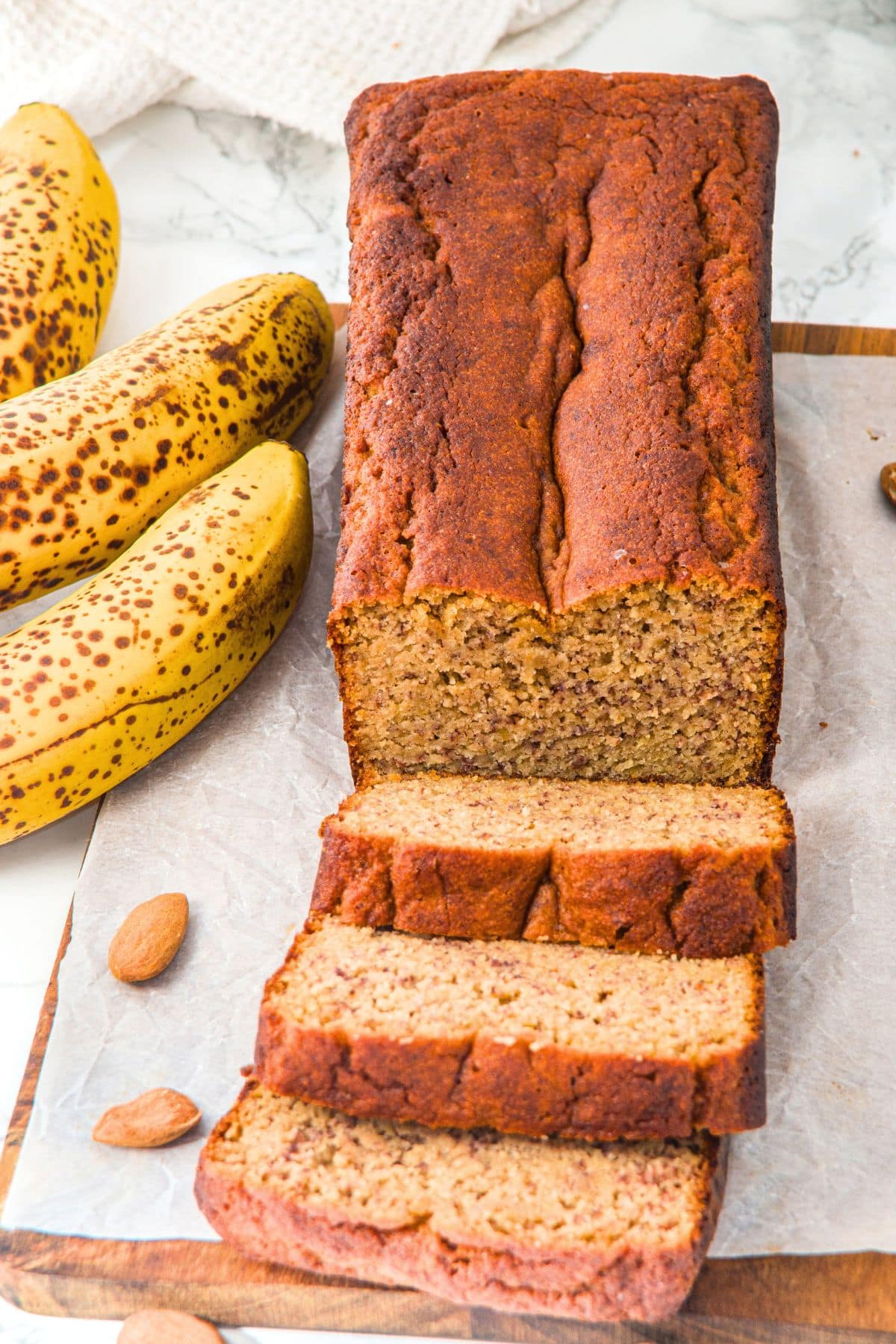 Sliced banana bread with almond flour on parchment-lined wooden board.