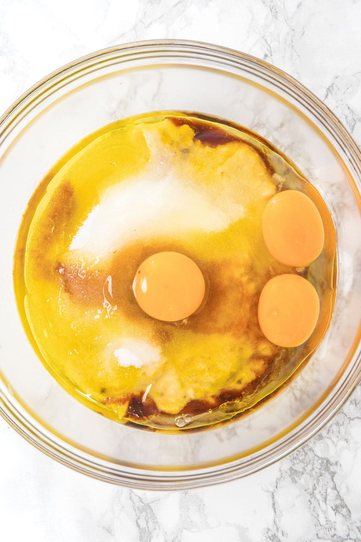 Eggs, sugar, vanilla extract, oil and mashed bananas in glass bowl.