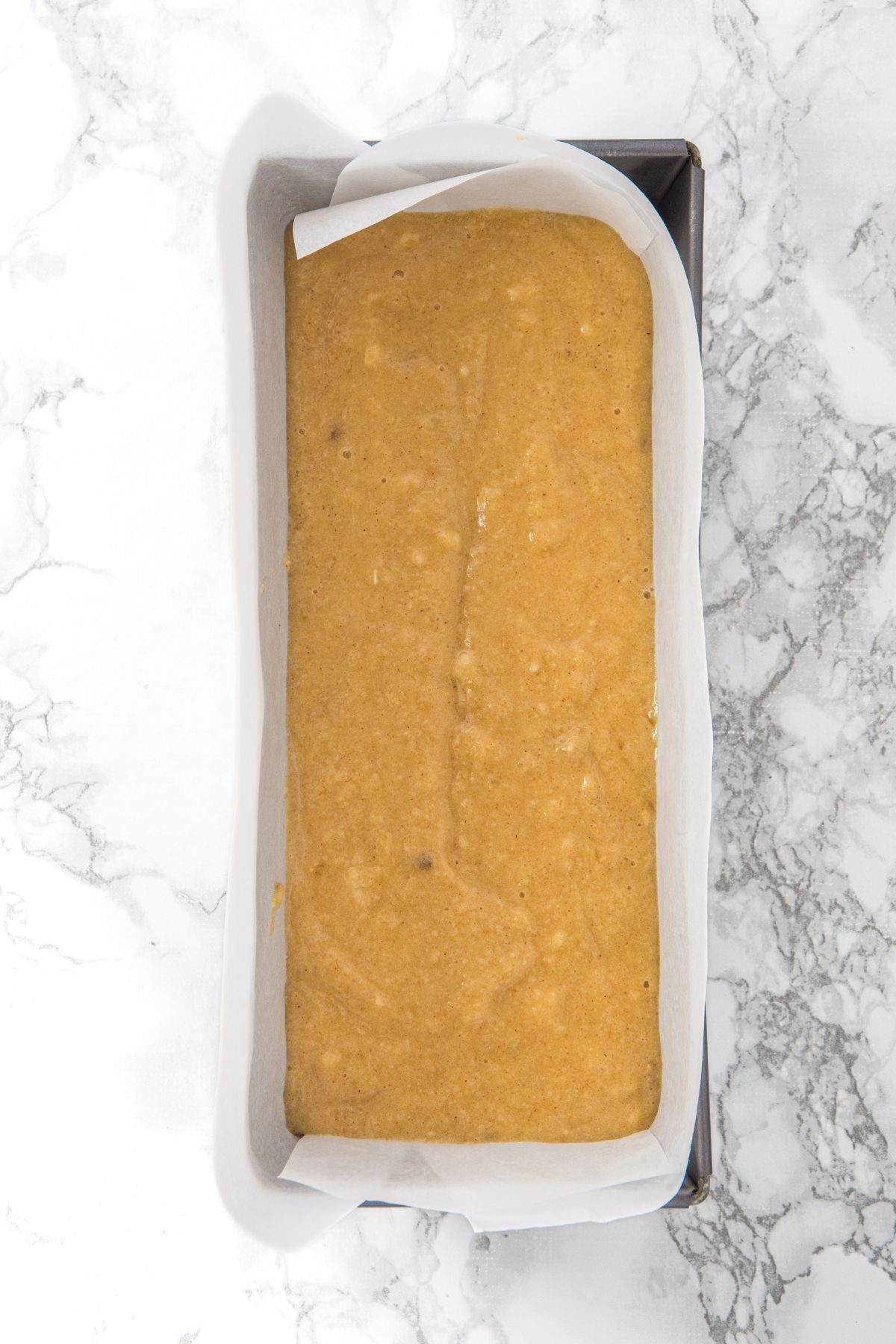 Banana bread batter in parchment-lined metal loaf pan