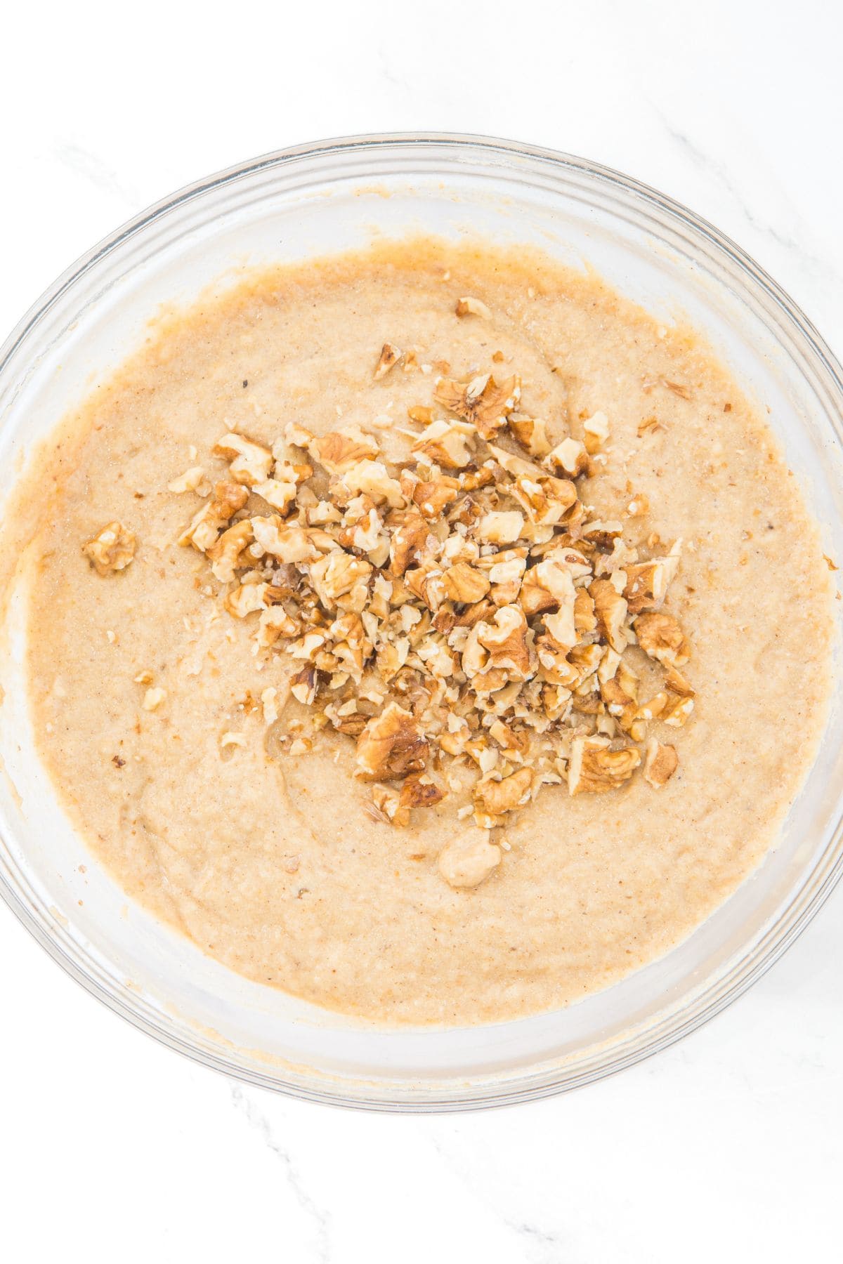 Chopped walnuts on top of pale brown batter in glass bowl