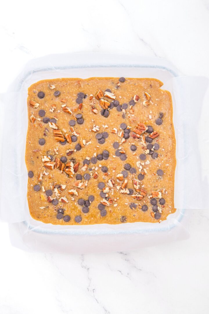 Blondie batter topped with chocolate chips and chopped pecans.
