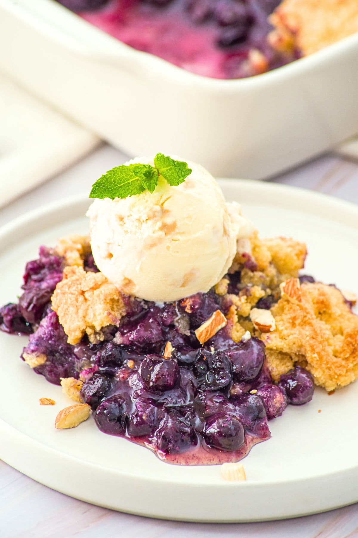 A portion of blueberry almond flour cobbler topped with vanilla ice cream.