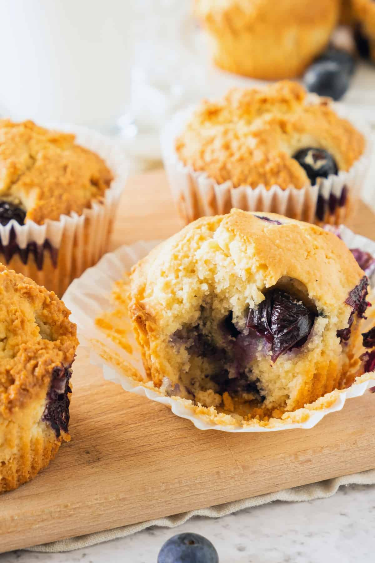 Half-eaten blueberry almond muffins on wooden board.