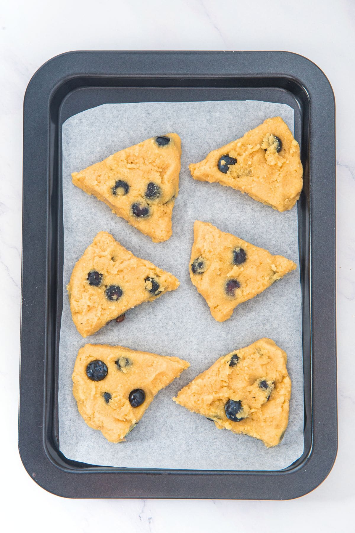 Triangles of blueberry scone dough on parchment-lined baking sheet.