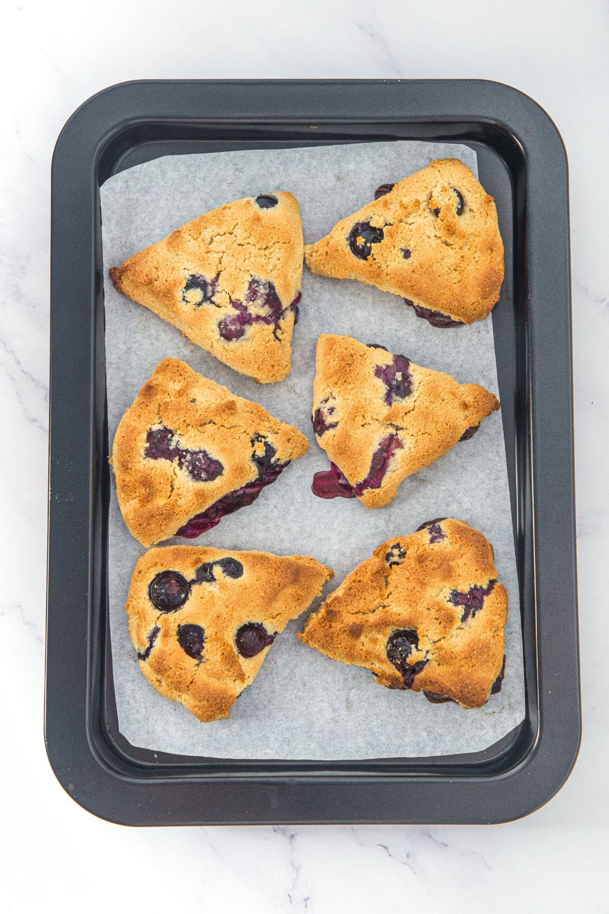 Freshly baked blueberry almond scones on parchment-lined baking sheet