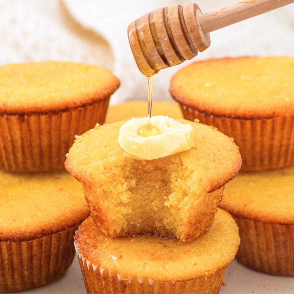 Drizzling honey over a stack of almond flour corn muffins