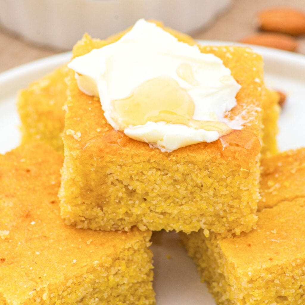 Up close view of almond flour cornbread topped with whipped cream and honey.
