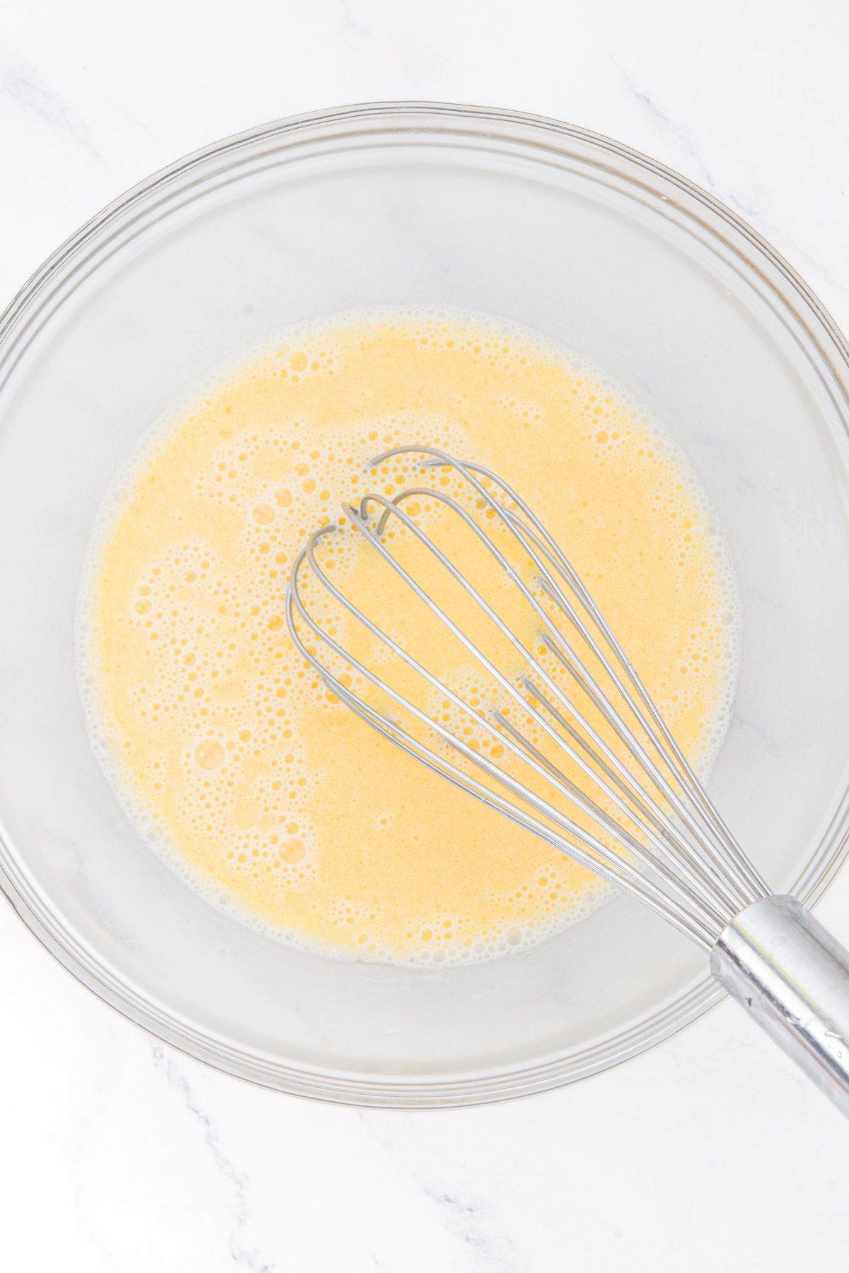 Whisking pale yellow liquid in glass bowl
