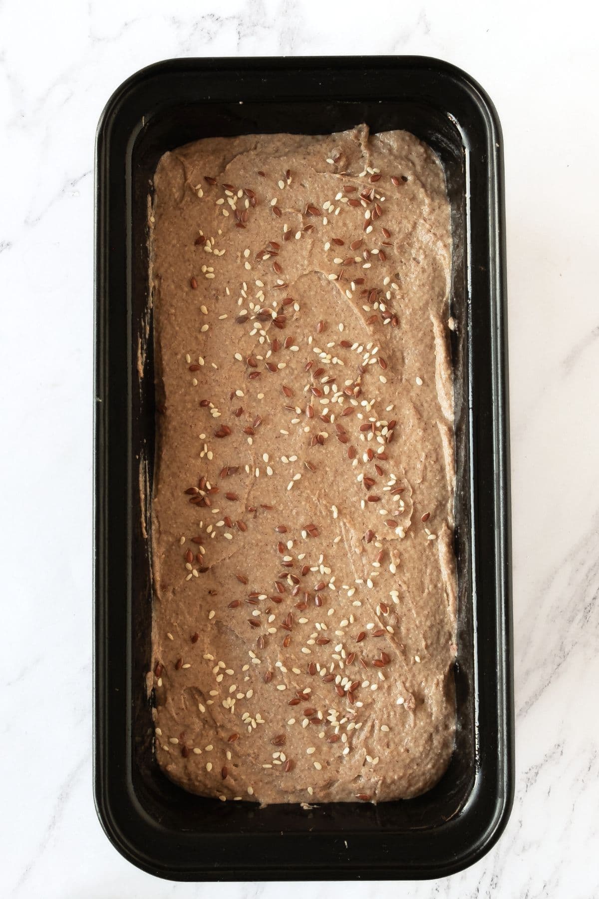 A metal pan with brown bread batter topped with brown and white seeds