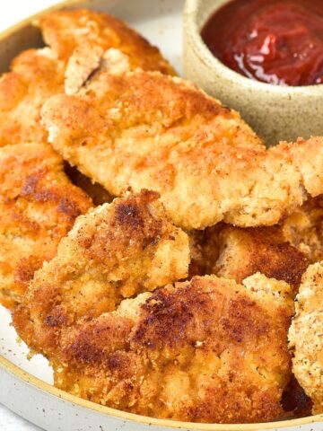 A plate of almond flour fried chicken next to a dipping bowl with ketchup