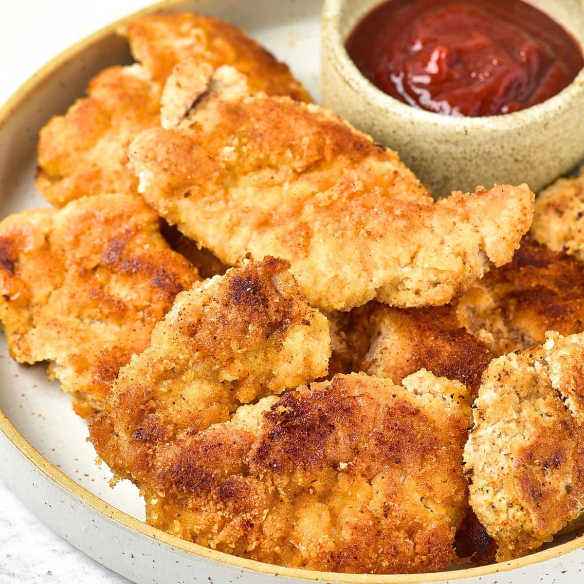 A plate of almond flour fried chicken next to a dipping bowl with ketchup