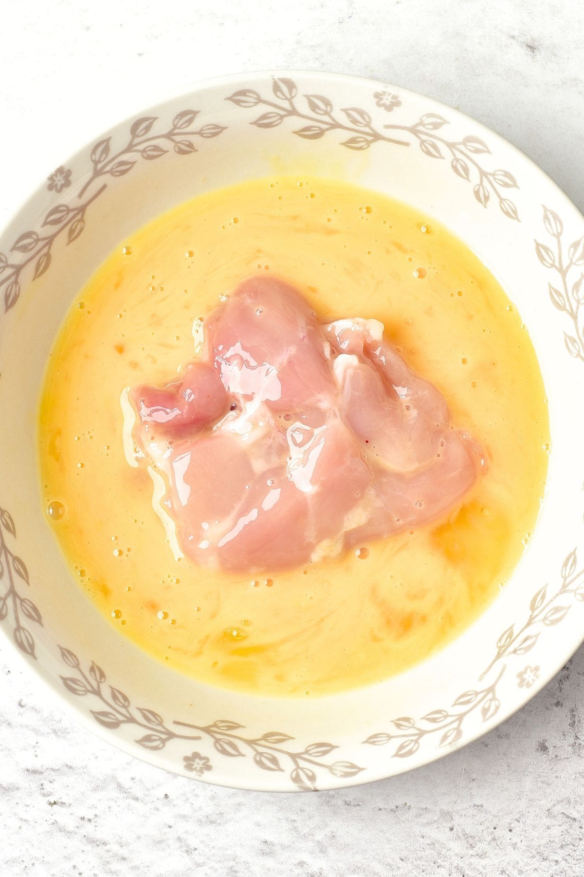 Dipping raw chicken thighs in beaten egg