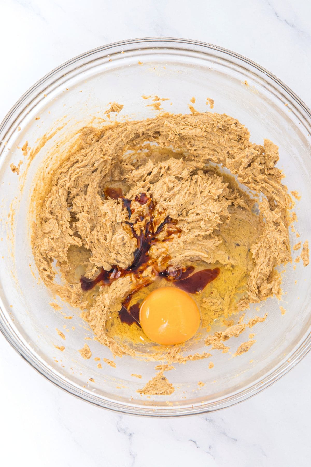 A bowl with beaten butter-sugar mixture topped with a raw egg