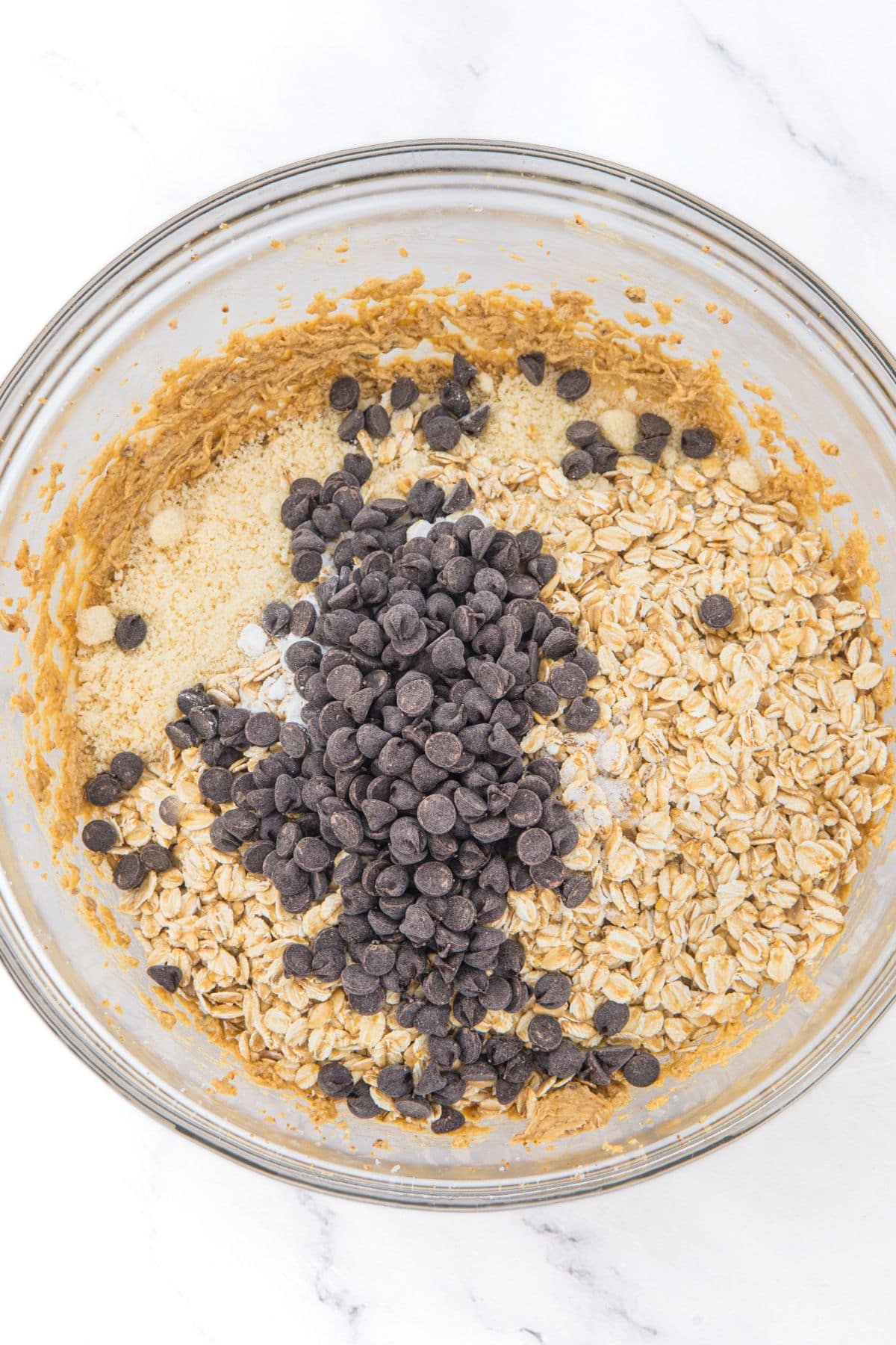 A glass mixing bowl with rolled oats, chocolate chips and almond flour