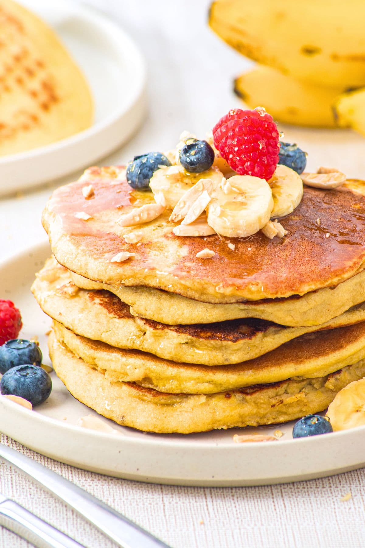 A stack of almond flour banana pancakes topped with fresh bananas and berries.