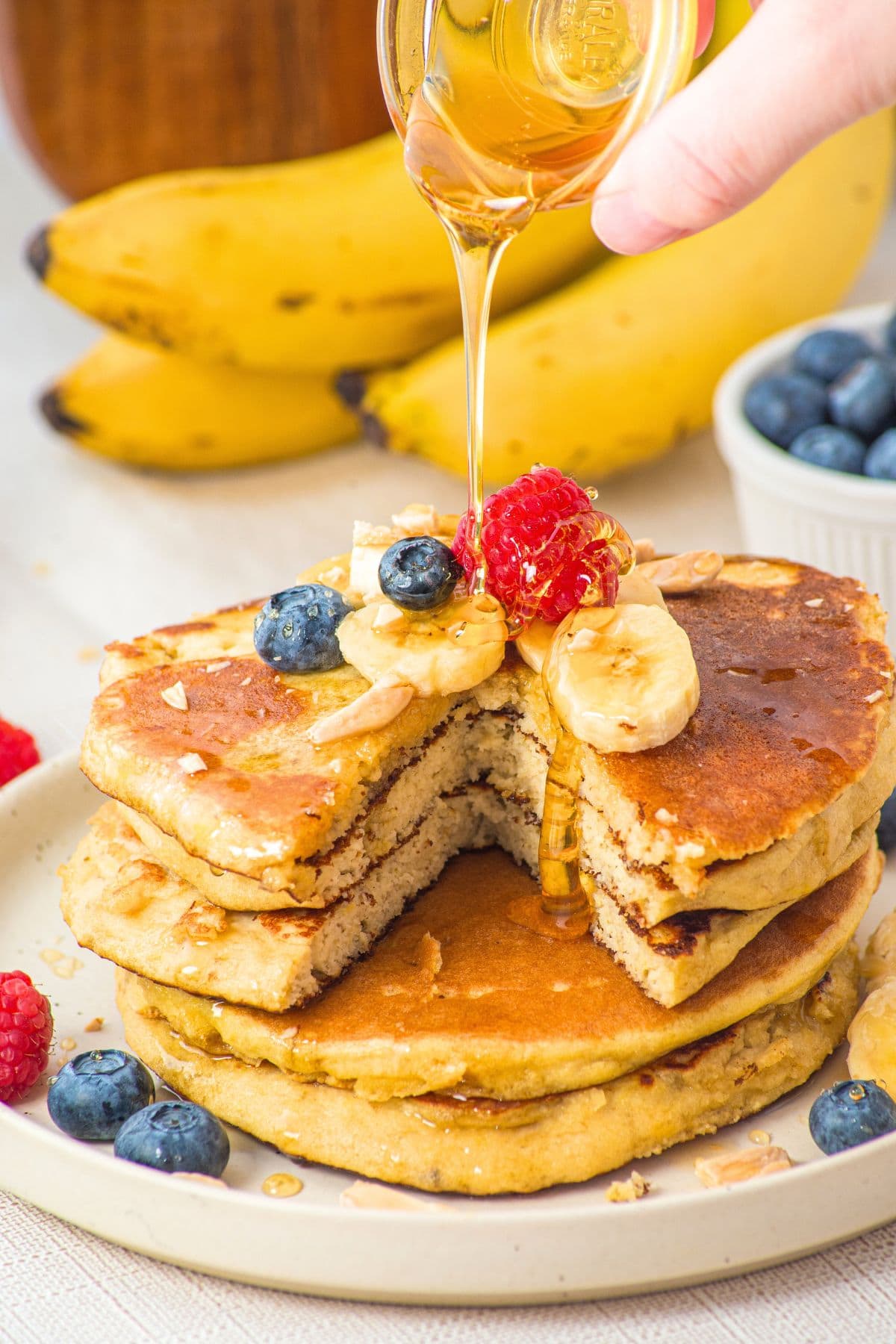 Drizzling maple syrup over a stack of banana almond flour pancakes