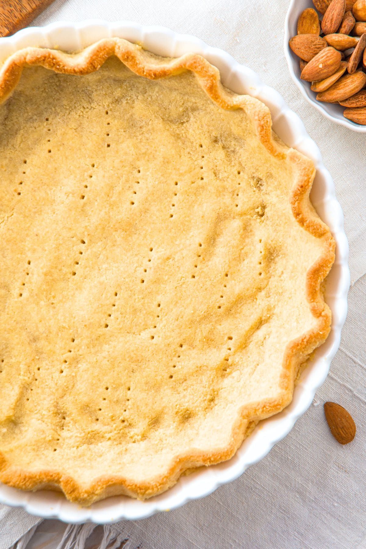 Top down view of freshly baked pie crust and bowl of almonds