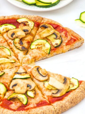 Half-eaten pizza with mushrooms and zucchini.