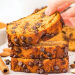 Hand reaching for a slice of almond flour pumpkin bread from a stack of slices.