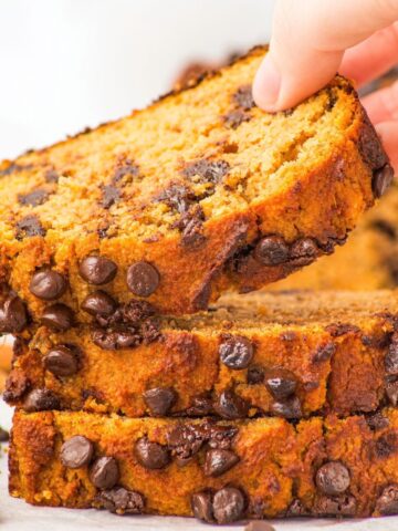 Hand reaching for a slice of almond flour pumpkin bread from a stack of slices.
