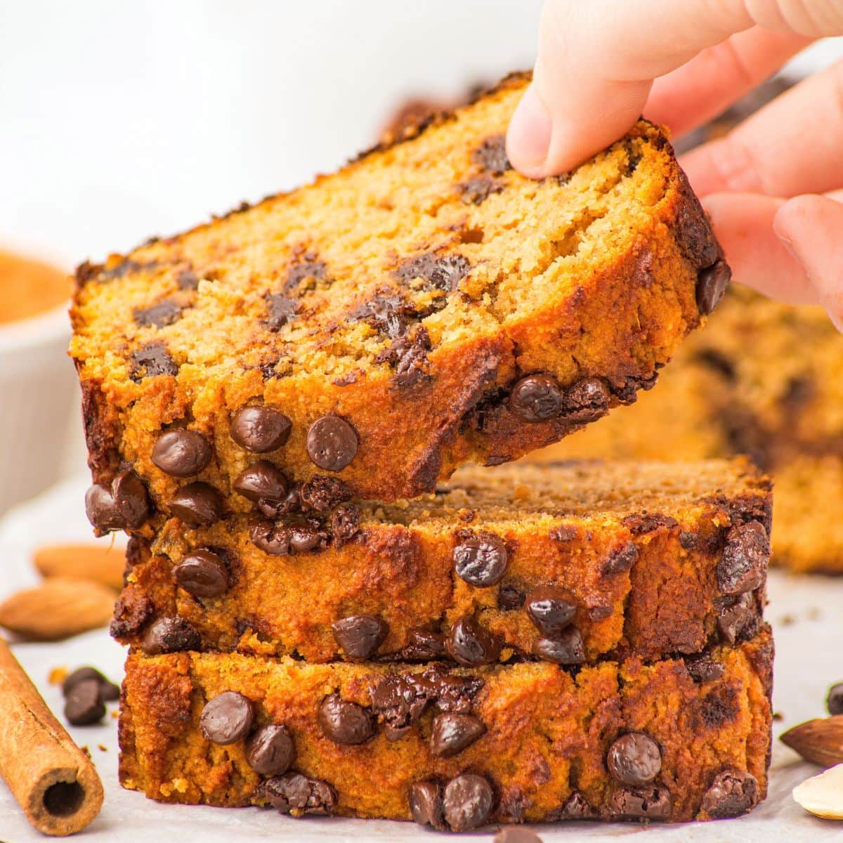 Hand reaching for a slice of almond flour pumpkin bread from a stack of slices.