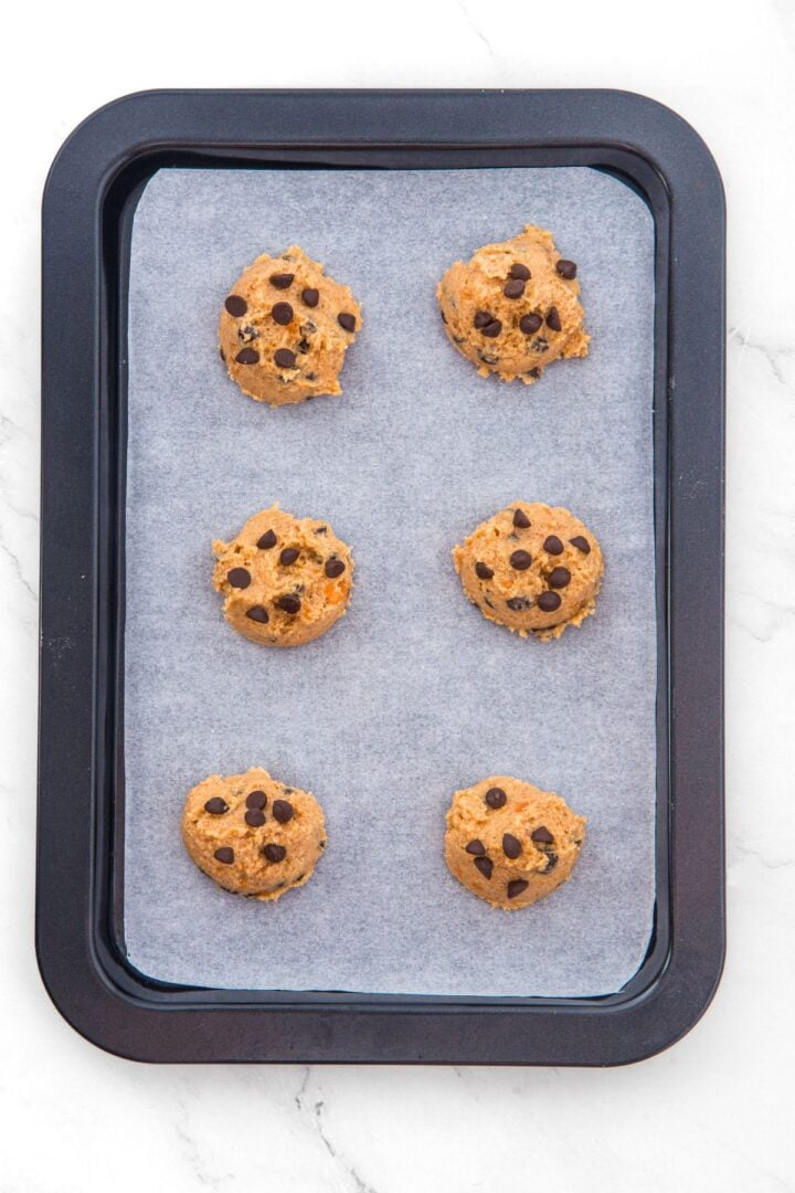 Top down view of balls of cookie dough on parchment-lined baking sheet.