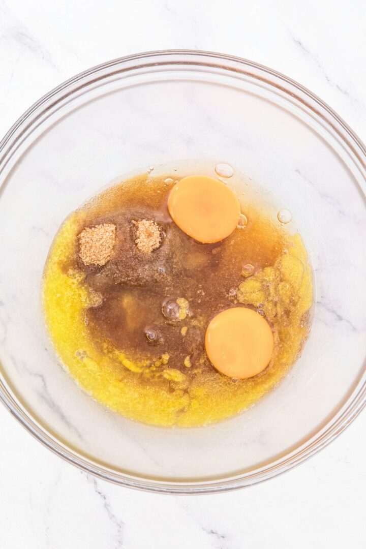A glass bowl with melted butter, eggs and brown sugar.