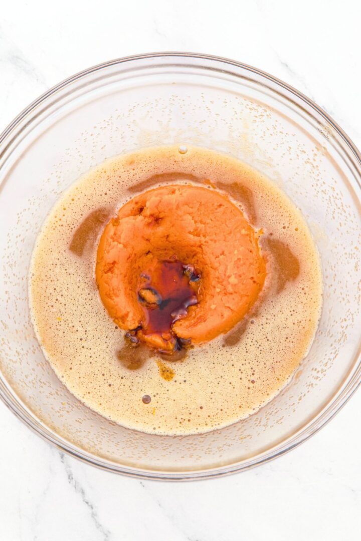 Brown liquid mixture and pumpkin puree and vanilla extract in glass bowl.